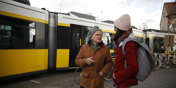 Ein älterer Herr und eine junge Dame unterhalten sich vor einer vorbeifahrenden S-Bahn